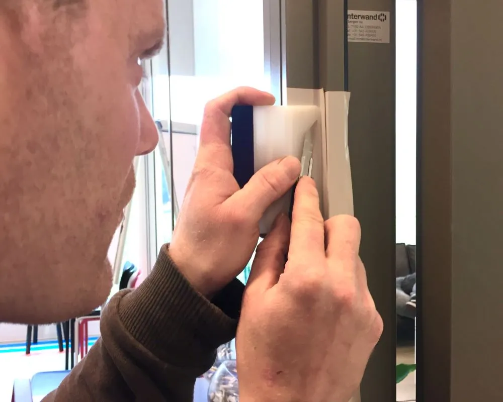 Cursist beplakt binnenhoek van een kozijn met Facadefilm kozijnfolie tijdens Facadefilm opleiding cursus “Schilderen met folie”