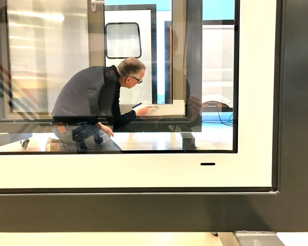 Cursist plakt Facadefilm kozijnfolie met rakel vast op aluminium kozijn tijdens “Schilderen met folie” Facadefilm training