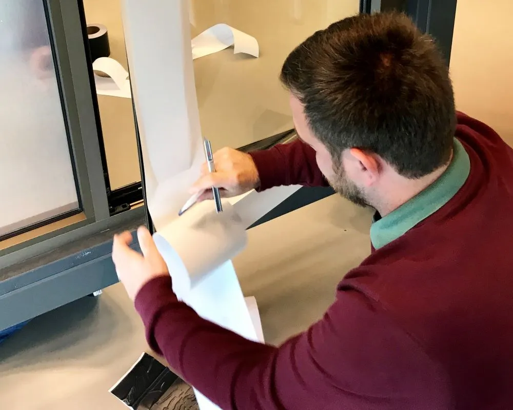 Cursist plakt Facadefilm kozijnfolie met rakel vast op aluminium kozijn tijdens “Schilderen met folie” Facadefilm cursus opleiding
