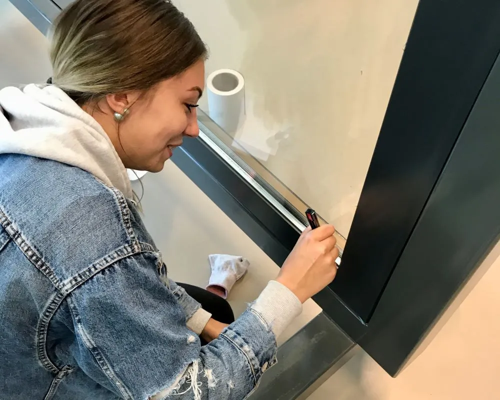 Cursist snijdt Facadefilm kozijnfolie met mesje af op aluminium kozijn tijdens “Schilderen met folie” Facadefilm cursus