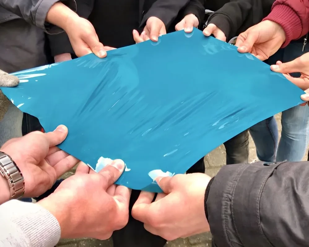 Handen van studenten middelbaar beroepsonderwijs houden samen stuk zelfklevende folie vast tijdens Appcademy gastcollege op ROC / MBO opleiding signmaker