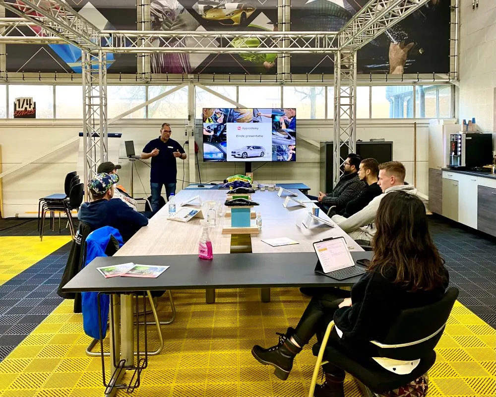 Trainer geeft info aan cursisten over raamfolie bij power point presentatie aan tafel tijdens Appcademy Automotive Windowfilm cursus