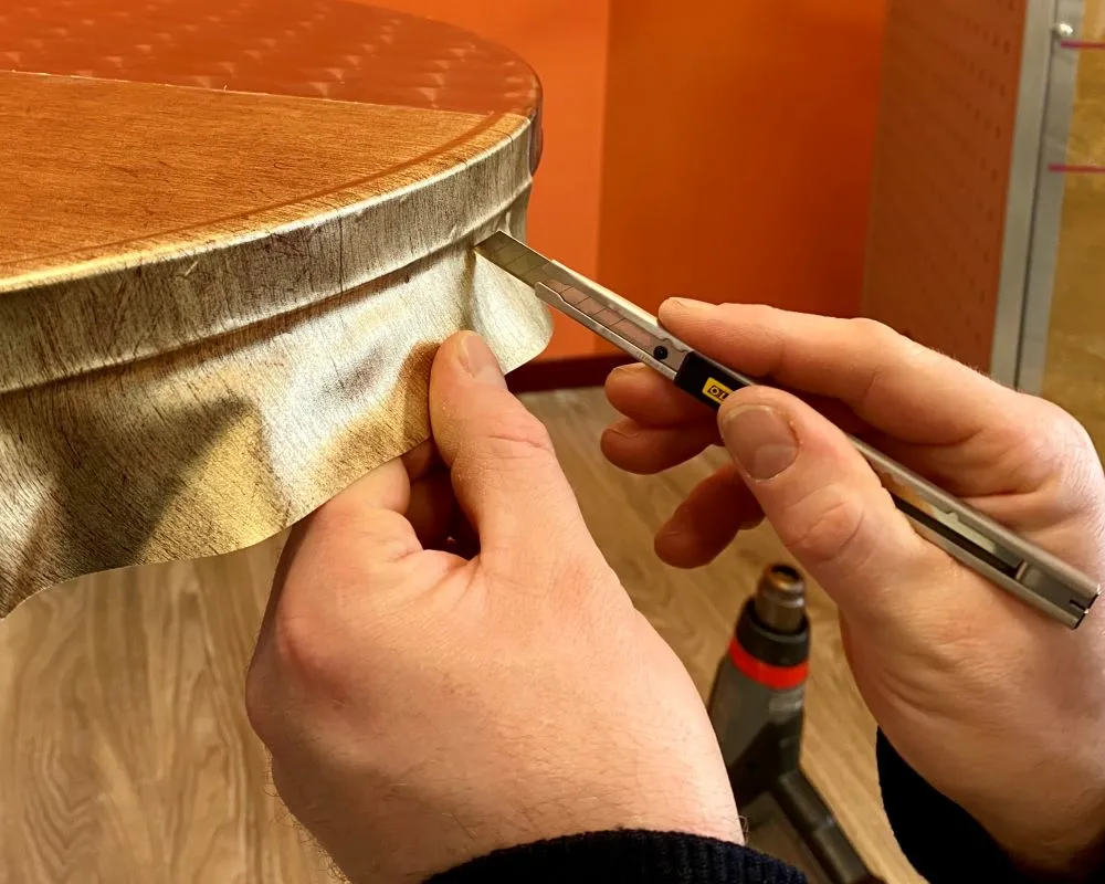 Cursist werkt de gewrapte zijkant van een bistrotafel af met snijtool als praktijkoefening tijdens de Appcademy training interieurfolies en keukens wrappen