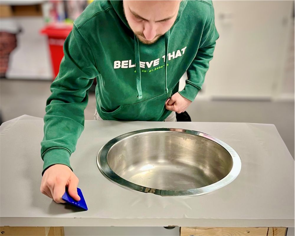 cursist brengt Interieurfolie aan op aanrecht rond de spoelbak tijdens de Appcademy cursus: Keukens Wrappen van A-Z